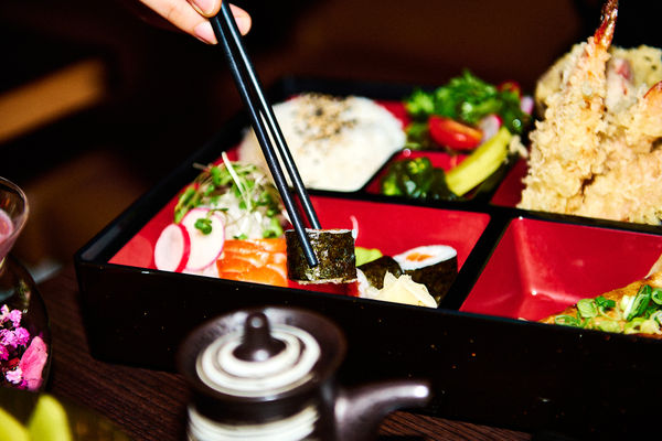 A bento box at Japanese restaurant with a person picking up a piece of sushi with chopsticks
