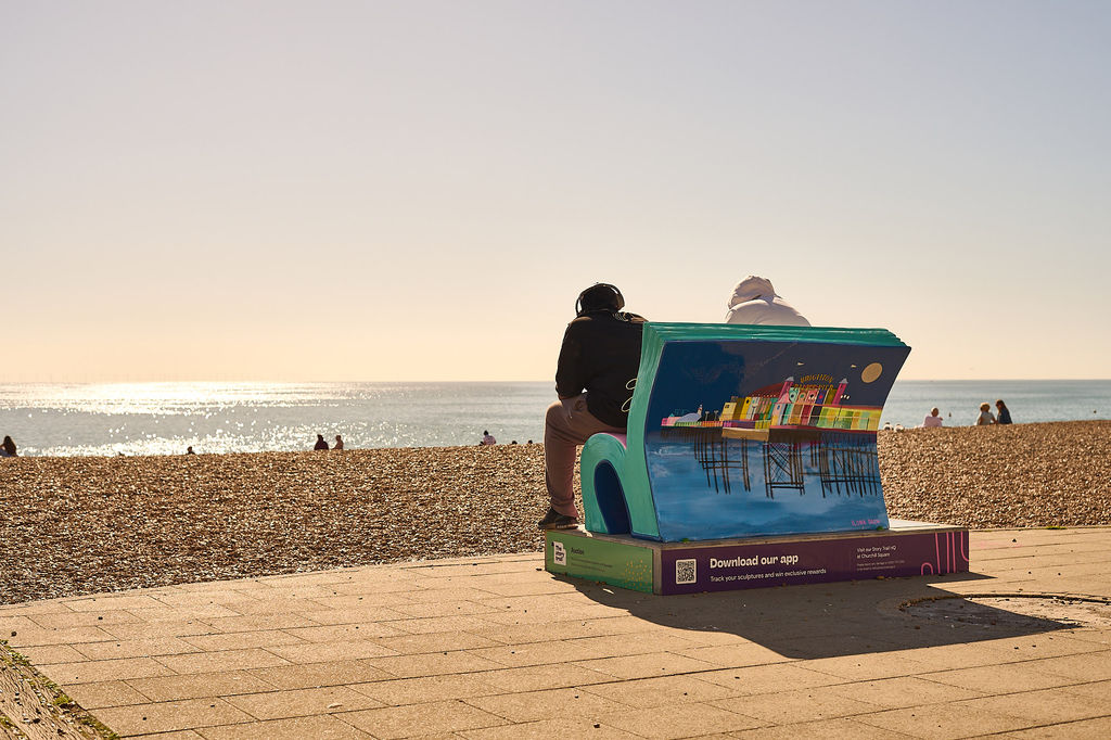 An illustrated Book Bench on Brighton seafront with two people sitting on the bench