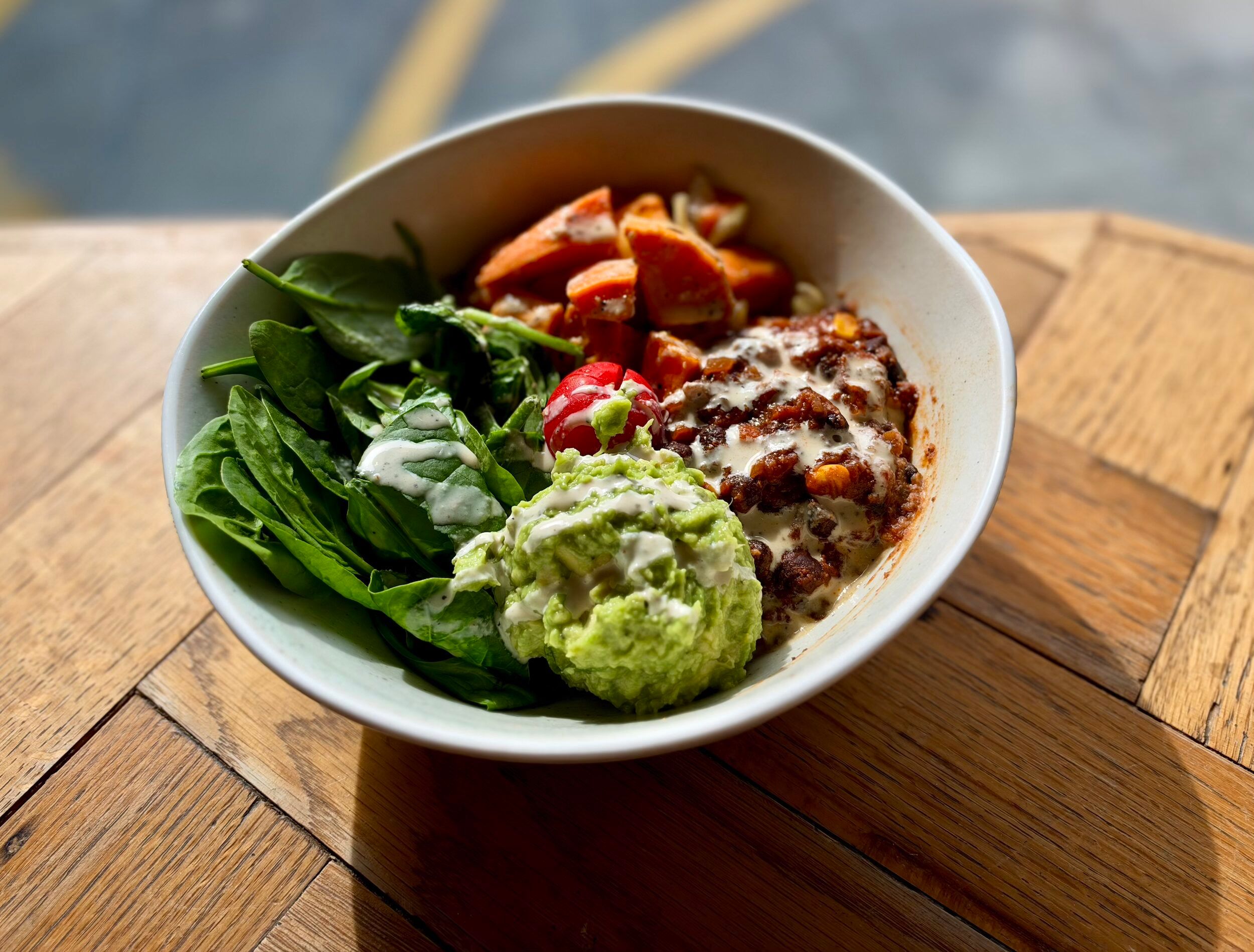 Sweet potato buddha bowl with roasted sweet potato, spinach, broccoli and beans on a wooden table at North Laine Café, Brighton
