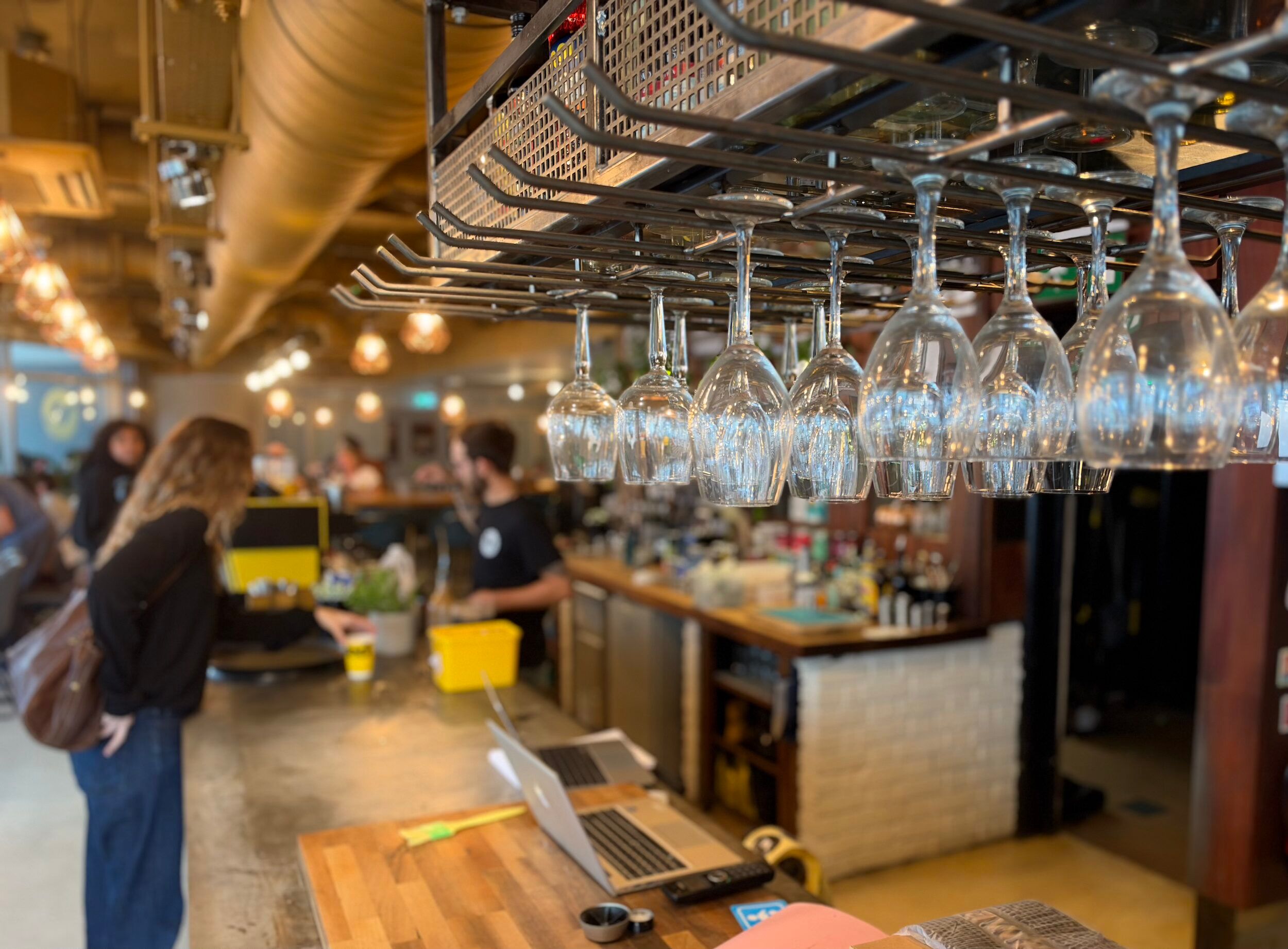 Rows of wine glasses hanging above the bar inside North Laine Café, Brighton, with staff and customers in the background