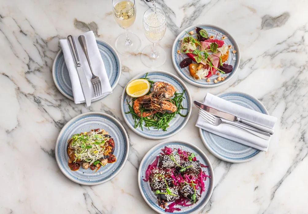 over head shot of someone pouring champagne into glass next to four different lunch dishes